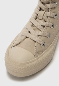 Baskets montantes en toile beige avec capuchon en caoutchouc, semelle texturée et œillets en métal pour les lacets. Présente des lacets tissés et un design cousu.