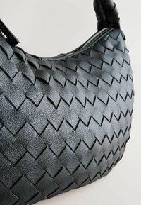 Černá tkaná kožená kabelka se složitým vzorem, zakřiveným tvarem a zipovým uzávěrem. Úchopy mají elegantní, hladký povrch.