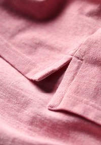 Różna tekstura materiału w kolorze różowym z kołnierzem z kątem nachylenia, sutami oraz miękkim, dzianinowym wyglądem.