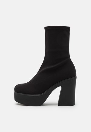 Botte noire mi-mollet à plateforme avec talon haut épais et bout arrondi, dessus en tissu lisse et bord supérieur élastiqué.