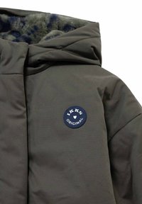 Donkergroene gewatteerde jas met een met bont gevoerde capuchon en een ronde blauwe patch met de tekst "IKKS Original" op de borst.