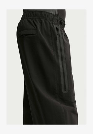 Crne hlače s elastičnim pojasom, s okomitim džepom na patentni zatvarač i džepom s preklopom sa strane bokova.