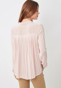 Blusa de color rosa claro con diseño de espalda plisada, mangas largas y collar. Tela suave con una silueta fluida.
