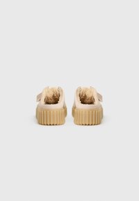 Beige fur-lined shoes with a textured ridged sole, featuring a back strap for support. The design is low-cut, providing easy wearability.