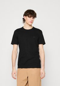 Čierne bavlnené tričko s krátkymi rukávmi, okrúhlym výstrihom a jemným logom "BOSS" na hrudi. Hladká textúra, klasický strih.