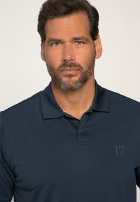 Mørkeblå polo t-shirt med struktureret overflade, to-knap lukning og et diskret logo på brystet. Har kontrasterende sort kravekant.