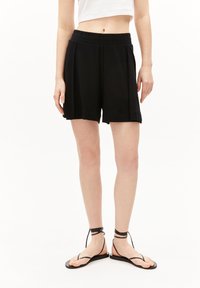 Zwarte, op de knie lengte shorts gemaakt van zachte stof met een elastische tailleband en geplooide ontwerp. Gepaarde met zwarte platte sandalen met dunne bandjes.