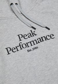 Grå hættebluse med sort broderet tekst "Peak Performance Est. 1986," med grå snører og en blød tekstur.