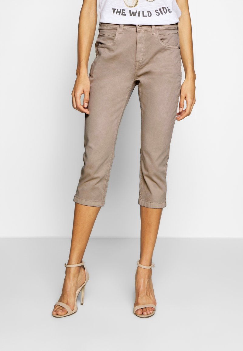 Mujer con pantalones cortos en taupe, tacones altos de tiras en beige y una camiseta blanca con un gráfico que dice "The Wild Side".