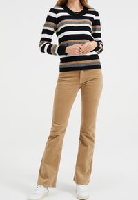 Stickad tröja med svarta, vita, beige och grå horisontella ränder; kombinerad med bruna kordflöjlsbyxor med utsvängd passform och vita sneakers.