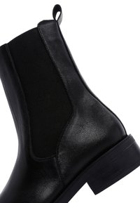 Bottine Chelsea en cuir noir avec une finition lisse, des panneaux latéraux élastiques et un petit talon carré. Comprend une languette à l'arrière.
