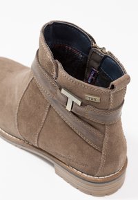 Bottine en daim marron avec une fermeture éclair latérale, des accents en cuir et un détail de logo en métal. Dotée d'une tige texturée et d'une semelle robuste.