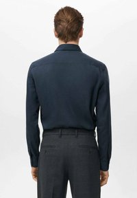 Camisa de manga larga azul marino con cuello clásico, textura suave y puños con botones, combinada con pantalones grises a medida que cuentan con bolsillos traseros.