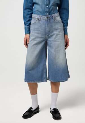 Blå denim culotter med en afslappet pasform, mellemhøj talje og vide ben. Har et falmet vask og færdige kanter. Bæres med sorte loafers.
