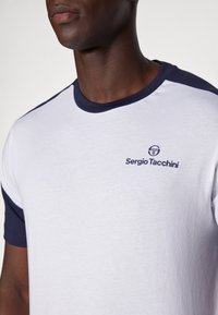 Witte katoenen t-shirt met marineblauwe accenten op de kraag en mouwen; heeft een klein geborduurd logo op de borst.