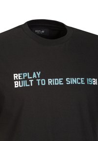 Schwarzes T-Shirt mit auffälligem Text: "REPLAY BUILT TO RIDE SINCE 1981" in Weiß und Hellblau, das einen lässigen, sportlichen Stil hervorhebt.