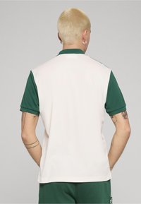 Koszulka polo z zielonymi rękawami i kołnierzem, białe тело. Charakteryzuje się klasycznym fasonem i gładką teksturą. Widok z tyłu nie pokazuje żadnych logo ani wzorów.