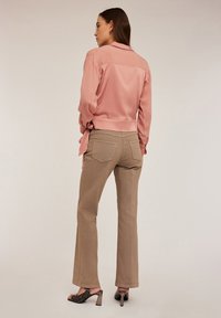 Lichtroze satijnen langetermijnshirt met een gestrikte taille, gecombineerd met taupe flared broeken met achterzakken en zwarte hoge hakken sandalen.