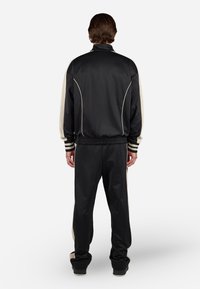 Chándal negro con acentos crema, que incluye una chaqueta con cremallera y cintura elástica, fabricado con material suave y ligero.