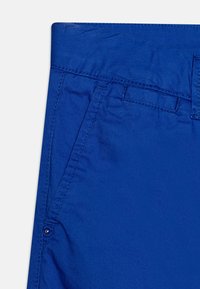 Pantaloni di cotone blu con una texture liscia, tasche laterali e dettagli di cucitura vicino all'elastico in vita. Sicuri per un abbigliamento casual.