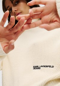 Cremfarbener Strickpullover mit strukturiertem Muster und oversized Passform. Mit gesticktem "KARL LAGERFELD JEANS"-Logo in Schwarz.