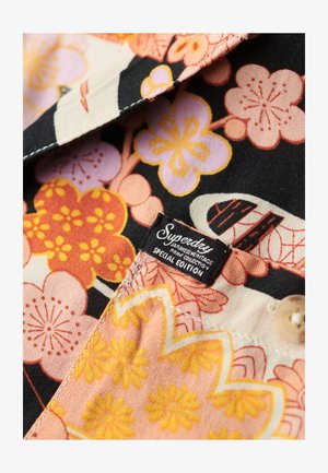 Stof met bloemenpatroon in roze, oranje en gele bloemen op een zwarte achtergrond. Bevat een "Superdry" label en een beige knoop.