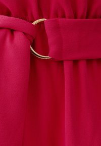 Magenta belt with a gold metal ring detail, made of soft, textured fabric. The fabric gathers at the waist for a fitted appearance.
