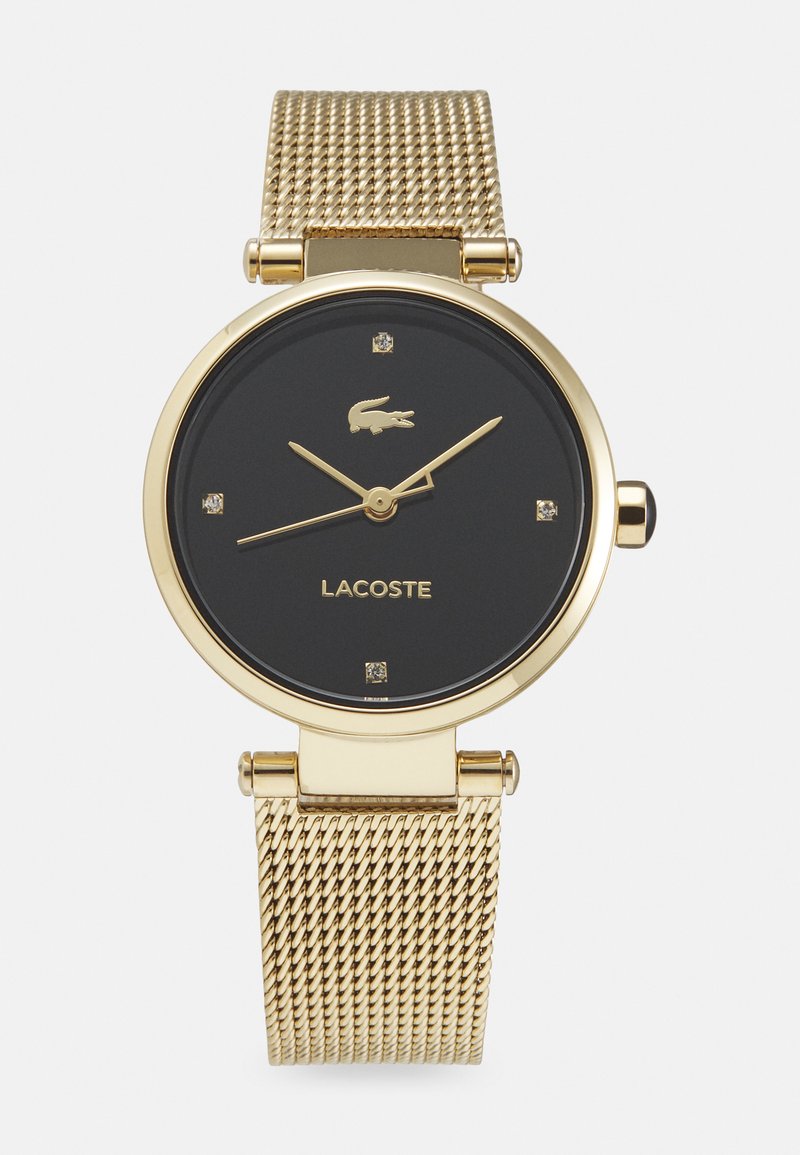 Montre bracelet en mailles dorées avec un cadran noir, ornée d'accents dorés, de quatre marqueurs semblables à des diamants et d'un logo. Boîtier rond au design minimaliste.