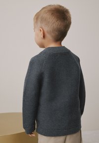 Pull en tricot gris foncé avec une texture subtilement côtelée et un col rond, vu de dos sur un enfant. Comprend un tissu doux et des manches longues.