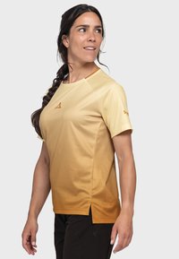 Hellgelbes Sportshirt mit einem Farbverlauf zu dunklerem Gelb. Kurzarm, Seitenschlitze, strukturiertes Material und ein kleines Logo auf der Brust.
