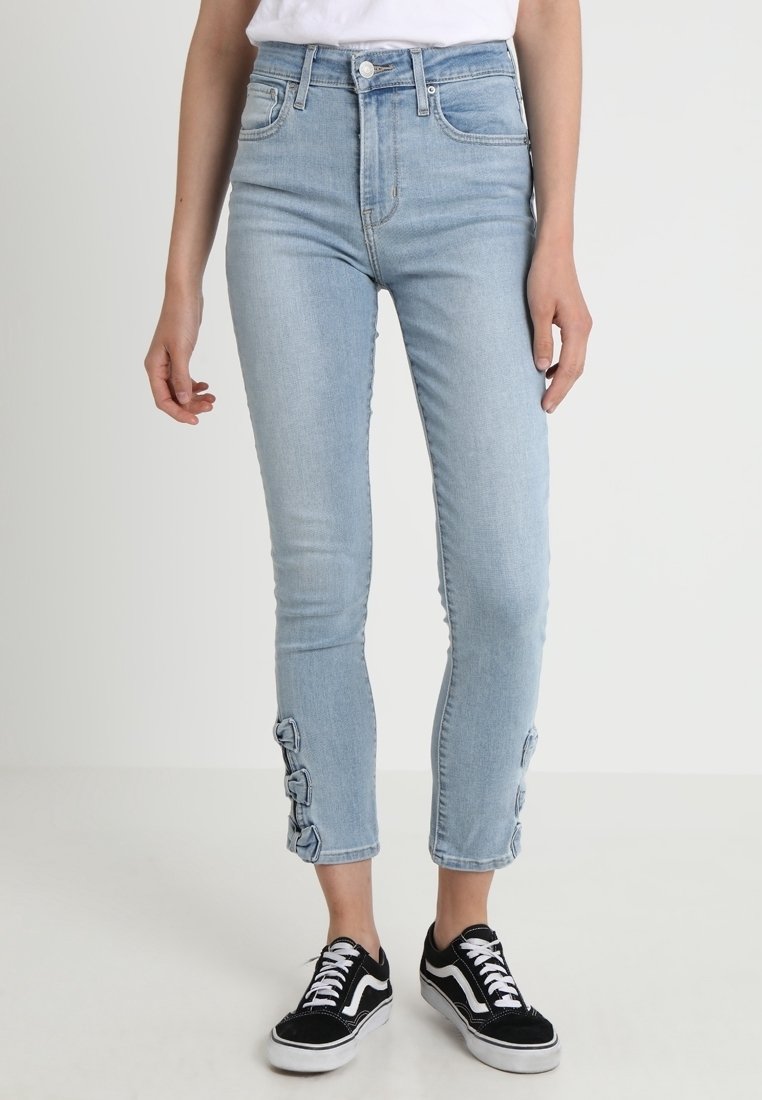 Ljusblå högmidjade jeans har en smal passform, ankellängd och ögla detaljer vid fållarna. Kombineras med svarta sneakers.