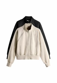 Conjunto de sudadera que incluye una chaqueta crema y una negra. Ambas tienen cierre de cremallera, cuello alto, mangas raglán y dobladillo de canalé. Tejido de textura suave.