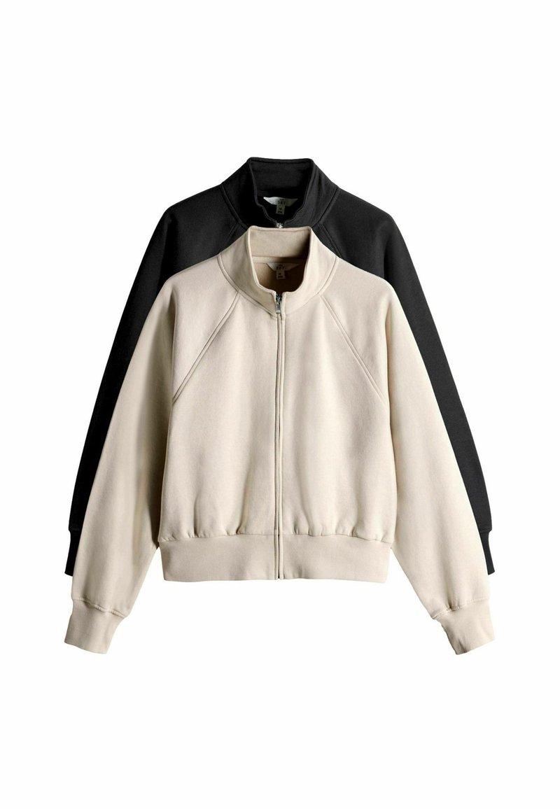 Conjunto de sudadera que incluye una chaqueta crema y una negra. Ambas tienen cierre de cremallera, cuello alto, mangas raglán y dobladillo de canalé. Tejido de textura suave.