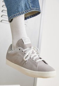 Sneaker grigio in suede con suola in gomma bianca, lacci tonali, dettagli perforati e logo adidas sulla linguetta, abbinato a un calzino bianco a coste.