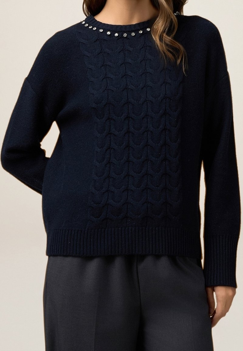 Pull en maille bleu marine avec un motif torsadé orné de strass décoratifs le long du col rond, des poignets côtelés et de l'ourlet.