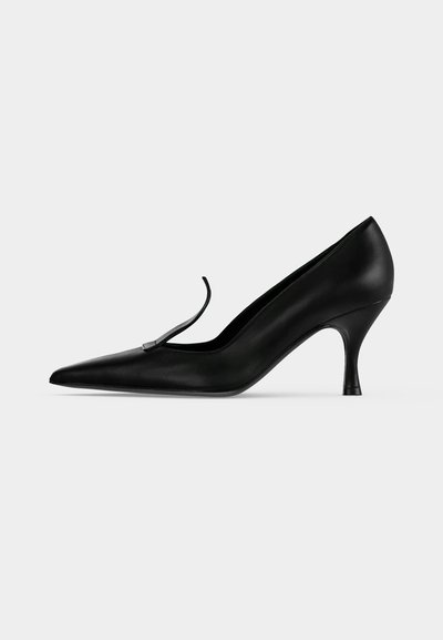 Chaussure à talon haut en cuir noir avec un bout pointu et une fine bride sur le dessus, vue de côté sur un fond uni.