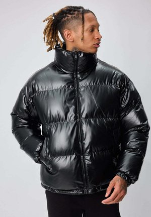 Doudoune noire avec une texture brillante et lisse, col montant, fermeture éclair et sections matelassées horizontales. Comprend des poches latérales.