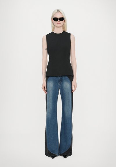 Schwarzes, ärmelloses Top mit schmaler Passform, kombiniert mit weiten Jeans aus Denim, die einen Farbverlauf von dunklem zu hellem Blau aufweisen und ein einzigartiges Split-Design haben.
