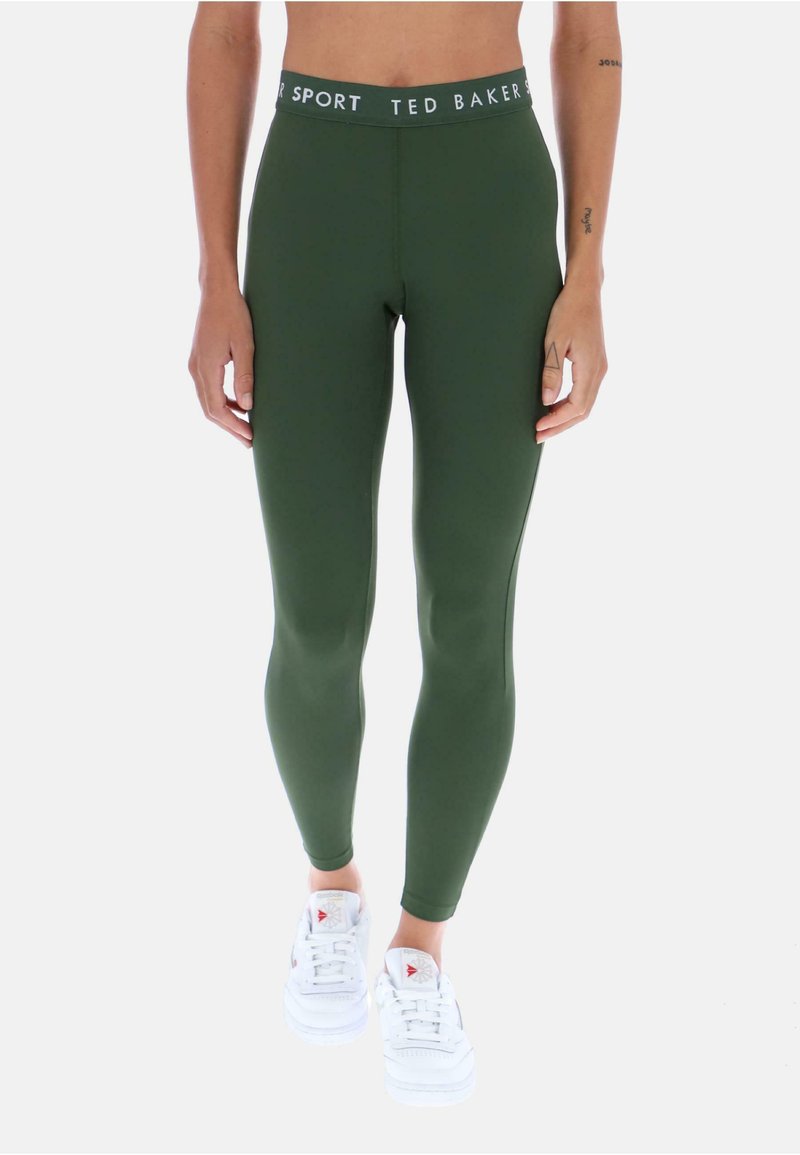 Zelené legíny vyrobené z hladkého a elastického materiálu, s bielym elastickým pásom s logom. Skombinované s bielymi teniskami.