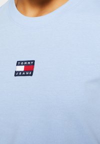 Ljusblått bomulls-t-shirt med en liten broderad Tommy Jeans-logga i rektangulär form i röd, vit och blå färg.