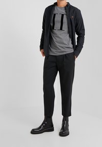 Sort skjorte med knapper over en grå T-shirt med en stor "II" grafik, kombineret med sorte tilspidsede bukser og skinnende sorte ankelstøvler.