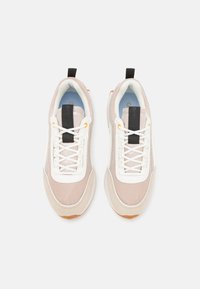 Lehké sportovní boty v béžové a bílé barvě s mesh svrškem, kontrastními černými akcenty a strukturovanou gumovou podrážkou. Mají zavazování na tkaničky.