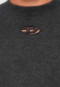 Κοντινό πλάνο σκούρου γκρι ριμπ πλεκτού πουλόβερ με οβάλ άνοιγμα και οριζόντια λεπτομέρεια μπάρας στο ντεκολτέ.