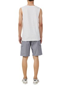 Witte mouwloze tanktop gecombineerd met grijze cargoshorts met zijzakken. Model draagt witte sneakers met grijze accenten.