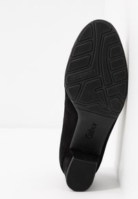 Semelle de chaussure noire avec adhérence texturée, détail "air cube" et marque "Gabor" sur les zones du talon et de la voûte plantaire.