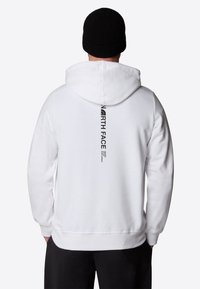 Vit huvtröja med huva, ribbade ärmslut och en svart vertikal logo på baksidan. Mjuk tygkvalitet med avslappnad passform och känguruficka.
