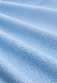 Helligblaue Stoff mit glatter Textur, der feine Strickmuster und einen leichten Glanz auf den gefalteten Flächen aufweist.