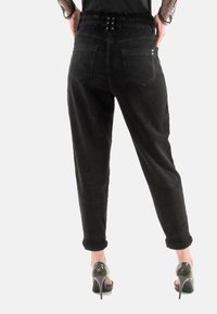 Pantalones de pana negra con un ajuste relajado, que cuentan con una cintura con cinturón, dos bolsillos traseros y puños enrollados. Combinados con zapatos de tacón alto.