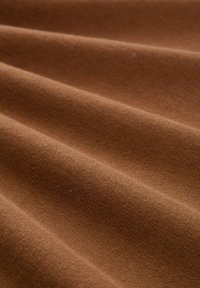 Tissu marron avec une surface douce et texturée, drapé en douces plis, mettant en valeur un tissage lisse et uniforme ainsi qu'une profondeur de couleur riche.