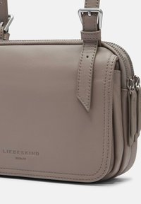 Borsa a tracolla in pelle grigia con hardware argentato, chiusura con zip e dettagli di cucitura sottili. Presenta una tracolla regolabile.